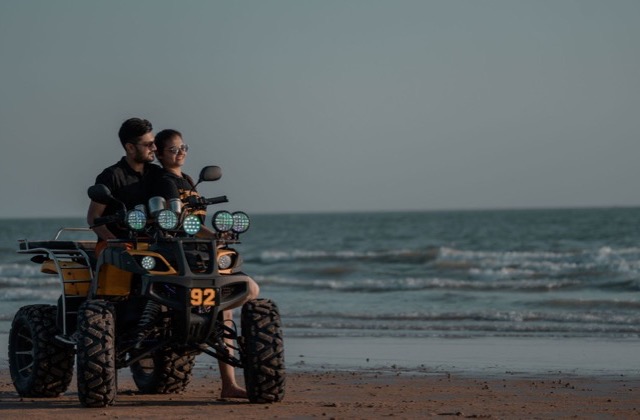 Two riders on a quad bike at the edge of a beach